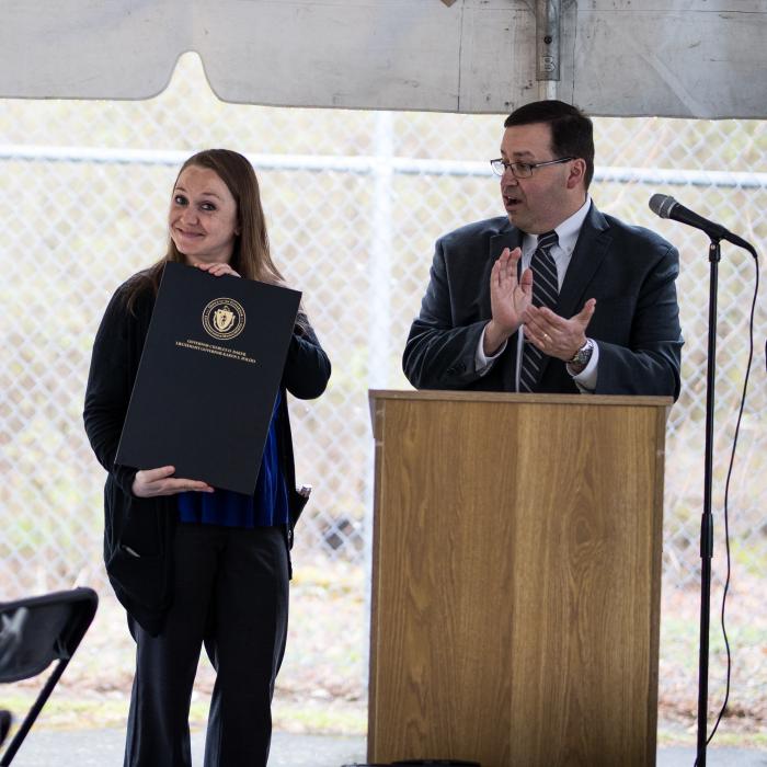 Courtney Edge-Mattos holds a the proclamation from the Governor while Michael Pay of DCF applauds at the podium.