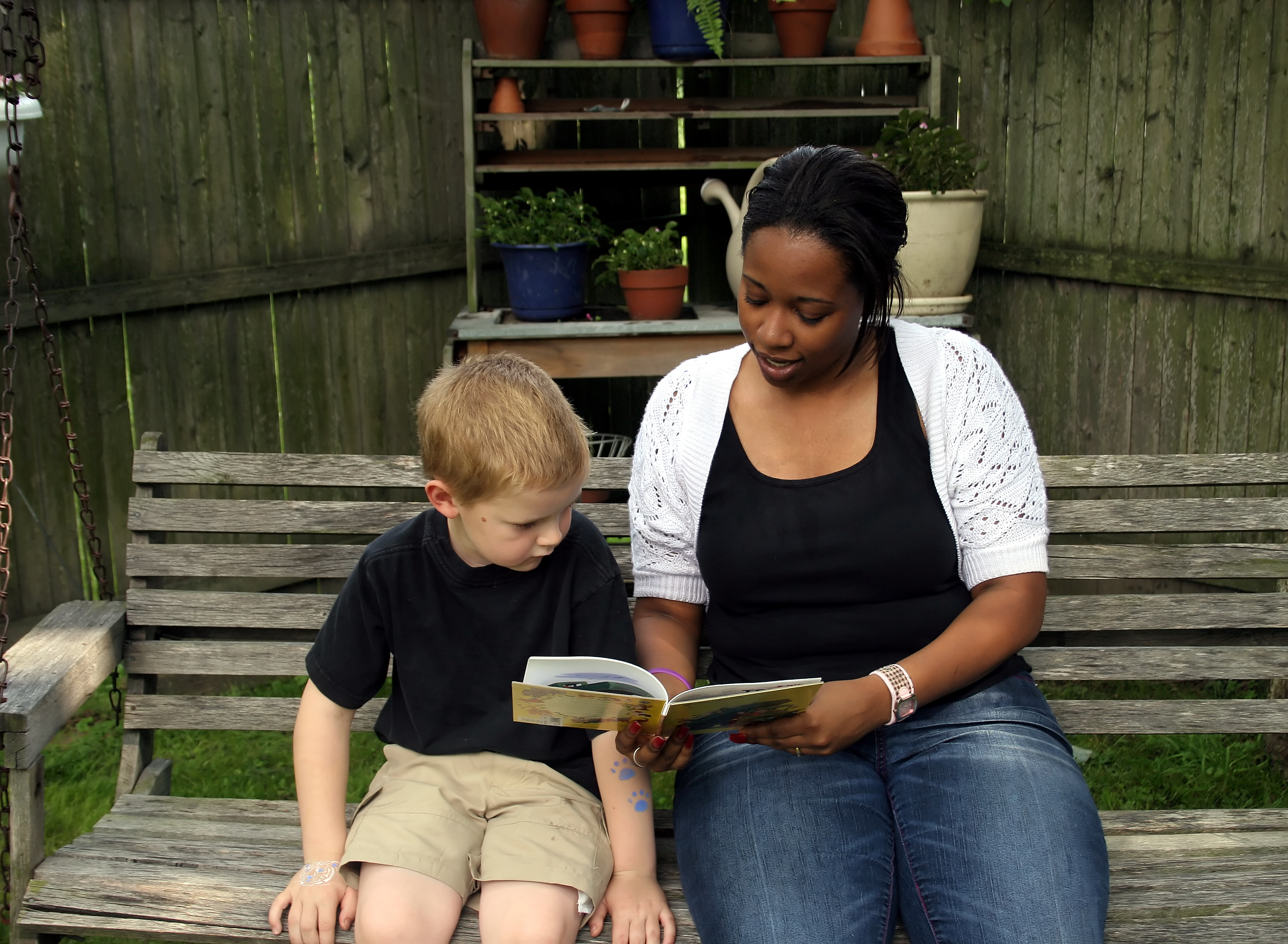 an african american woman and a young child sitting on a bench reading