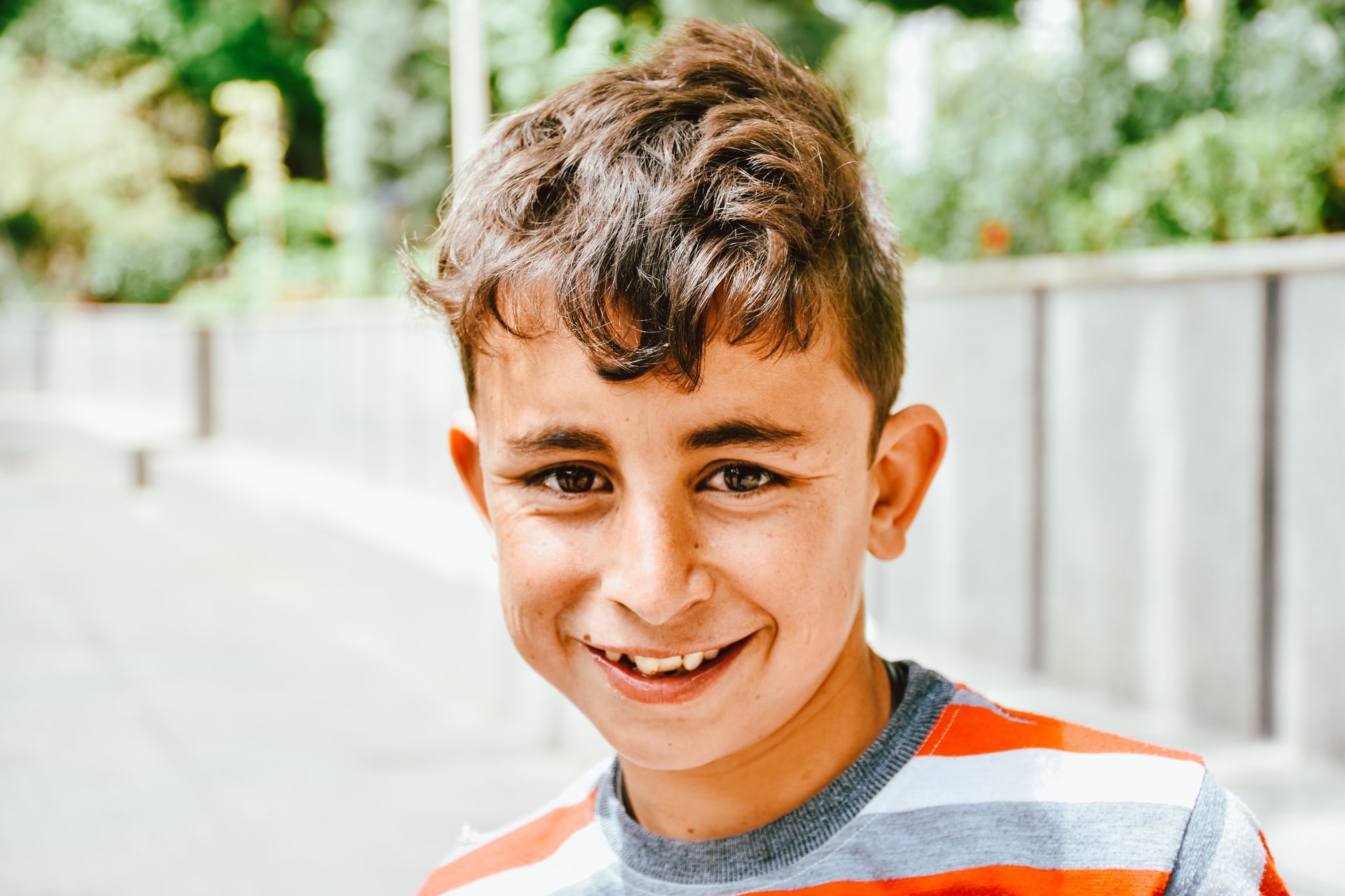 A middle school aged boy in a striped shirt smiles at the camera.