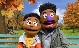 two puppets of color sitting on a park bench