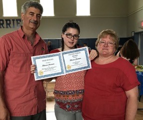 Theresa holds her awards while standing with her parents