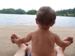 baby holding onto adult feet on beach