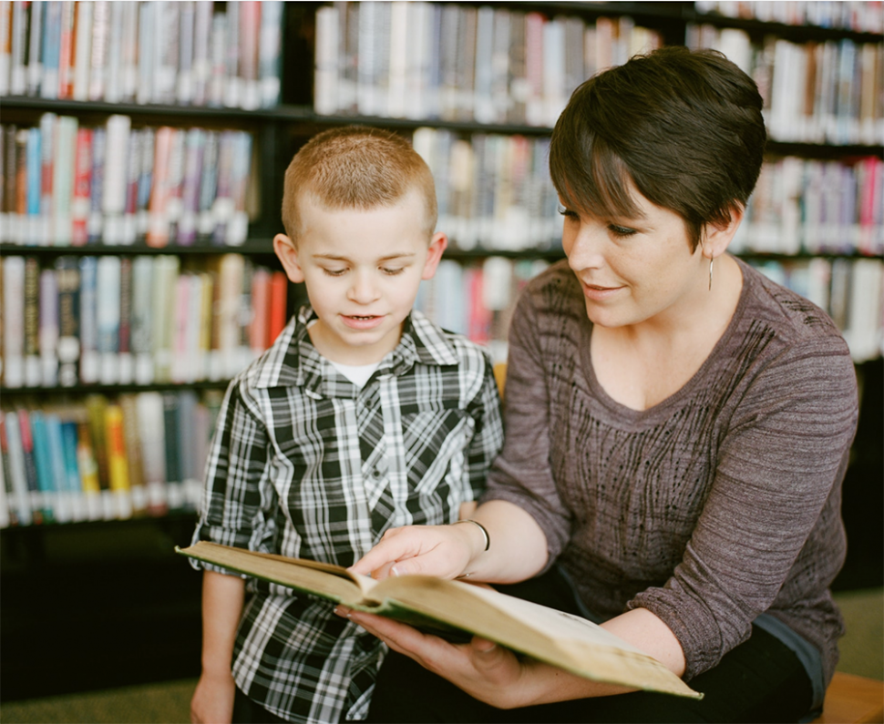 adult female reading a book to a young child at a library