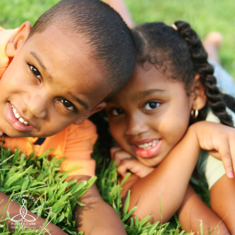 A brother and sister of African ancestry smile at the camera and pose on a grassy lawn.