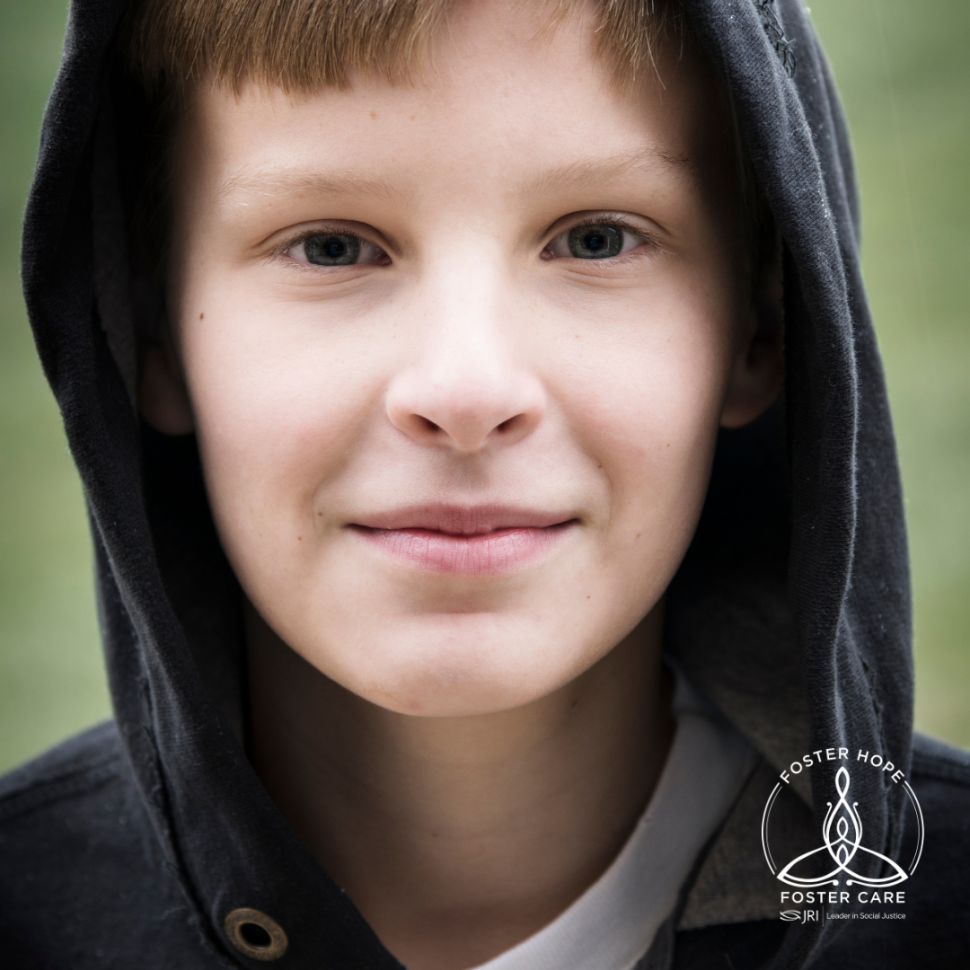 Caucasian pre-teen boy wears a black hoodie sweatshirt and smiles shyly at the camera.