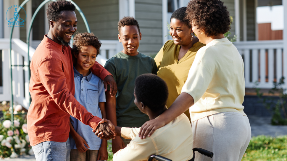 A family stands outside on a sunny day.  There are four adults, one of whom is in a wheelchair, and two young teen boys.  They are all smiling and greeting each other.