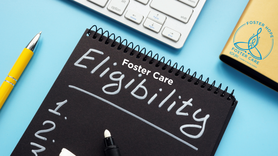 A blue desk features a yellow pencil, part of a computer keyboard in view, a black pad of paper that says "Eligibility" and a gold notebook with the JRI Foster Care logo embossed on the cover.
