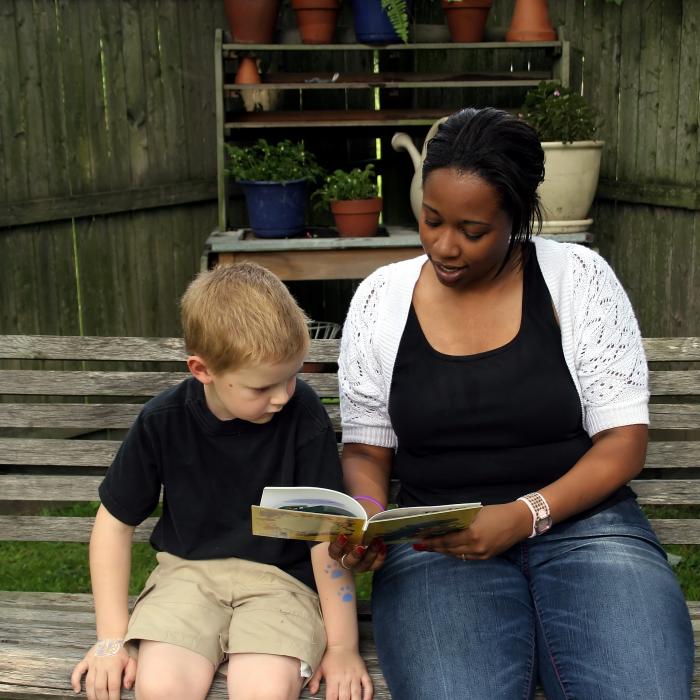 an african american woman and a young child sitting on a bench reading