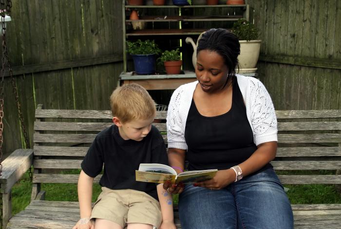 small child approximately 5 years old and their caregiver reading a book on a bench