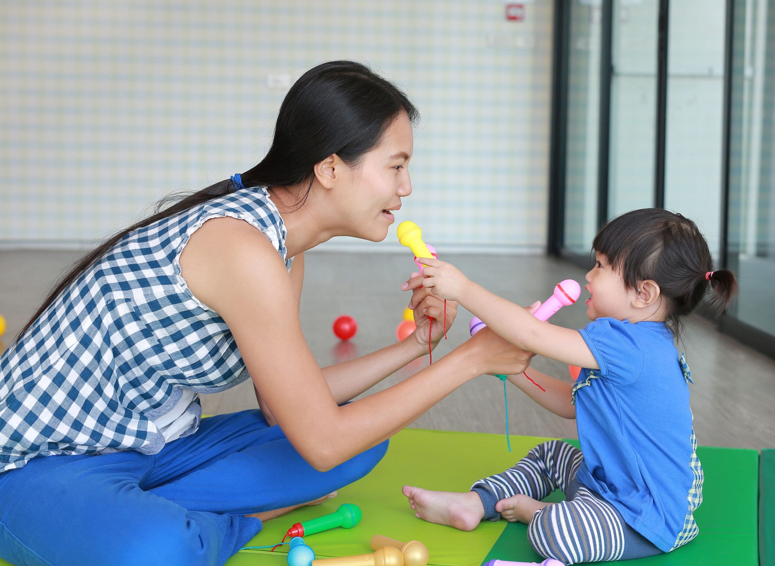 Mother and daughter playing with colorful toy microphones indoors.