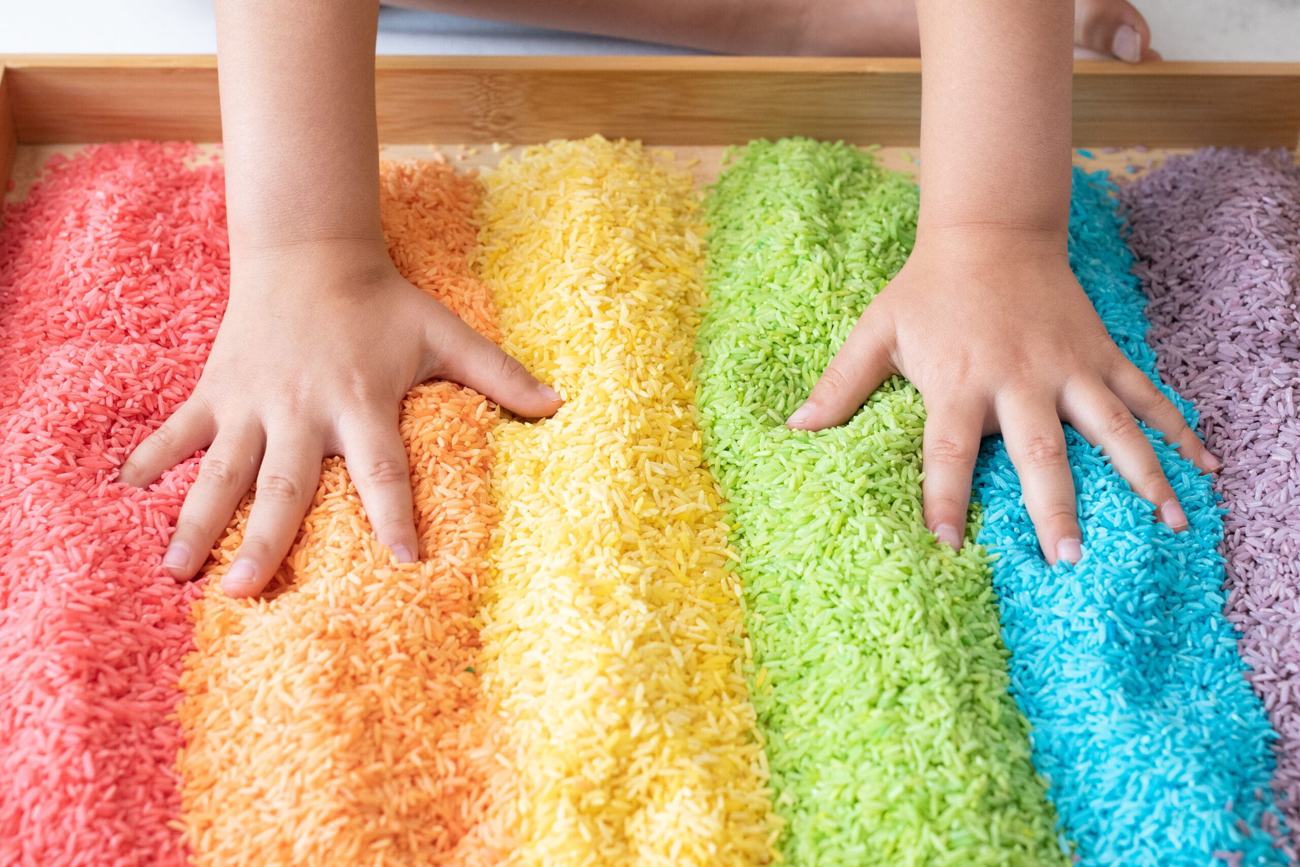 Child's hands in rainbow-colored rice sorted in sections.