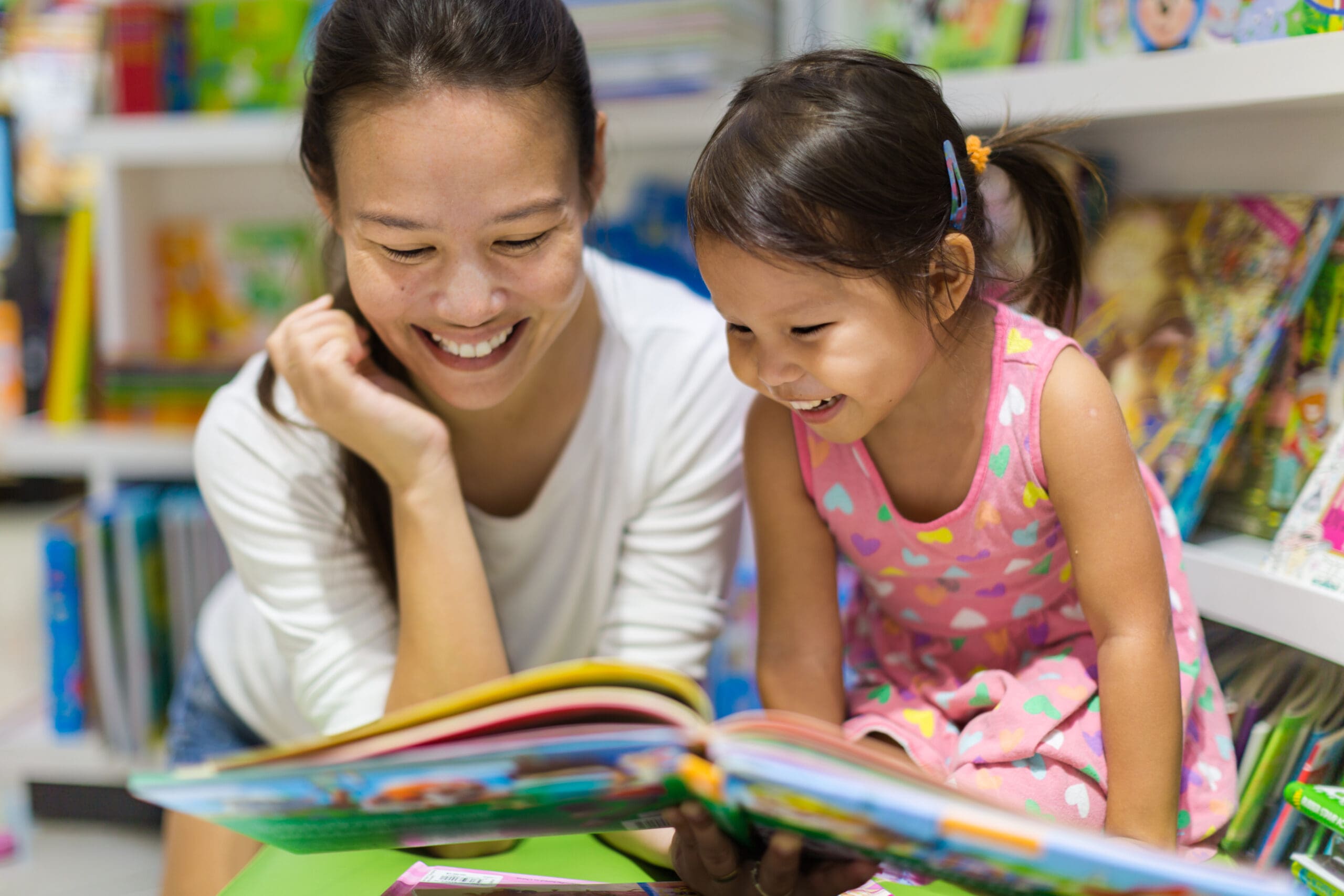 Mother and child reading a colorful book together in a library