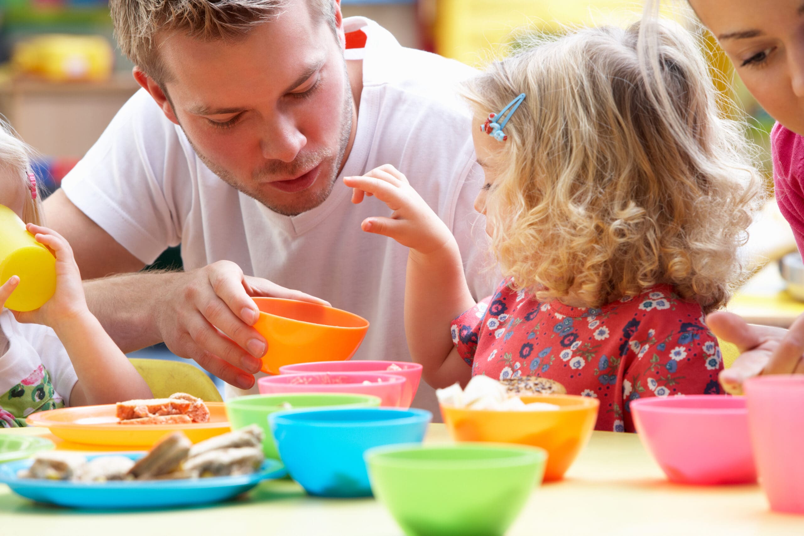 Adult with children around a table with colorful bowls, engaging in activity.