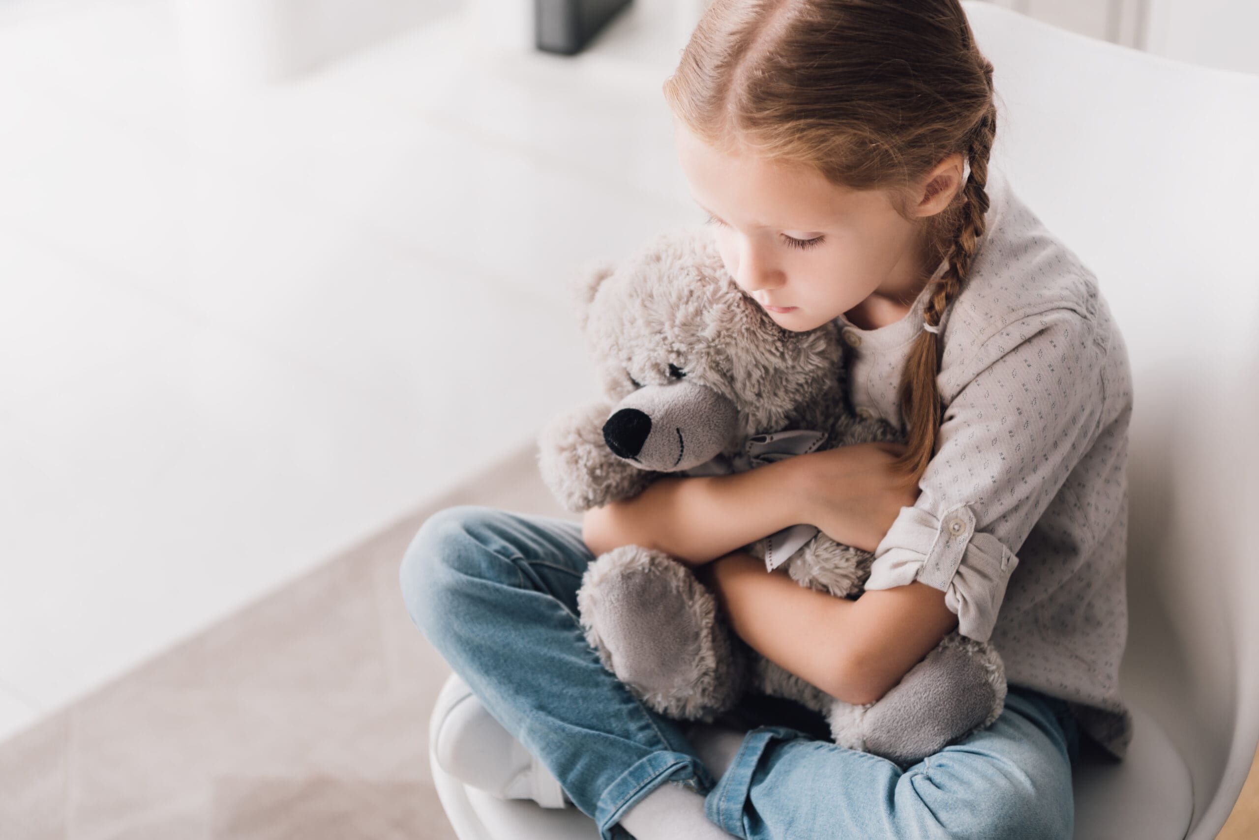 Girl holding a teddy bear, sitting on a chair.