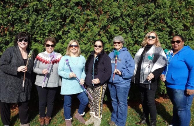 Group of seven people outdoors in front of green trees.