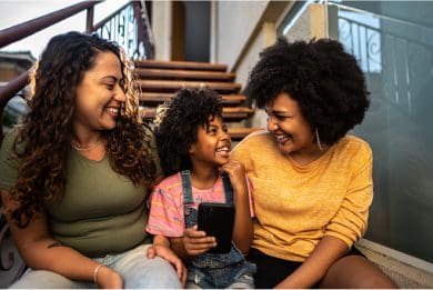Family of three sitting on stairs, smiling and interacting with a phone.