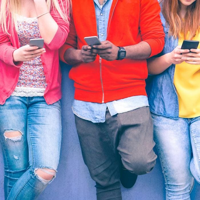 Three people looking at smartphones, close together, casual clothing.