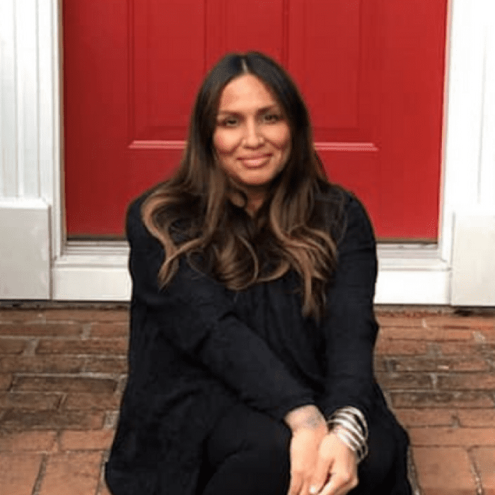 Portrait of Christina Valila sitting on steps in front of a red door, smiling.