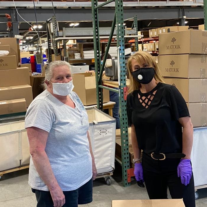 Two individuals wearing masks in a warehouse with boxes around them.