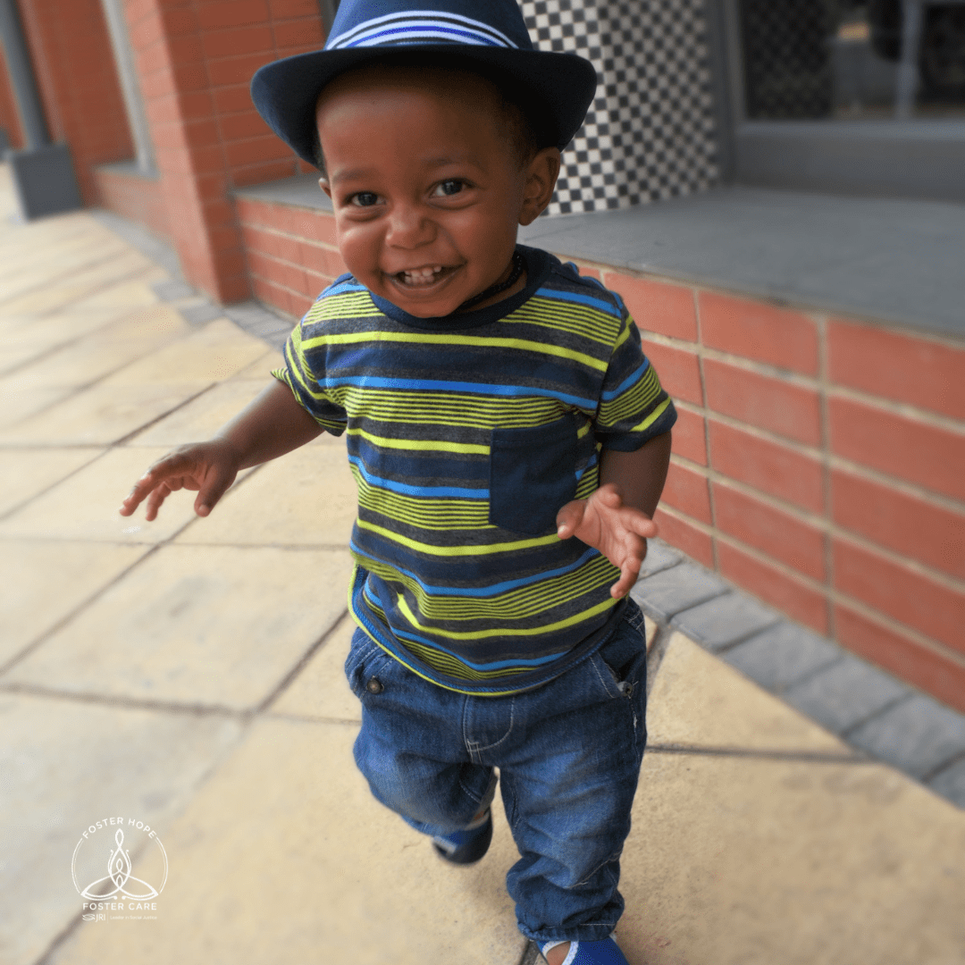 Young child smiling and running outside, wearing a striped shirt and hat
