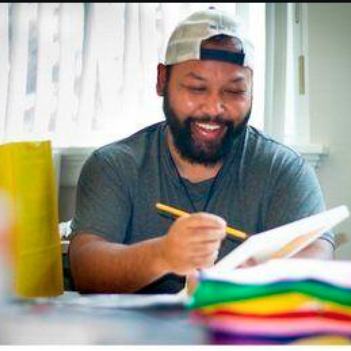 Person smiling while writing in a notebook with colorful papers nearby