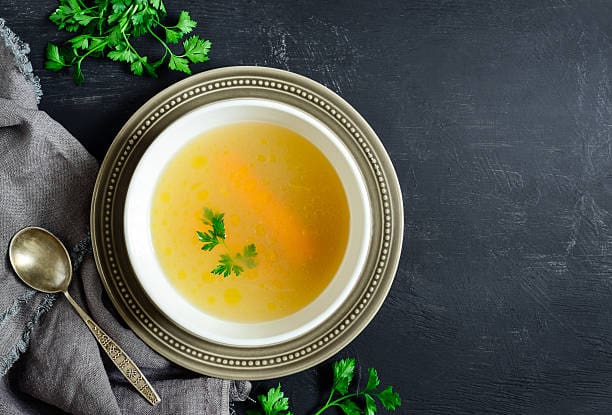 Bowl of broth garnished with herbs on a table.
