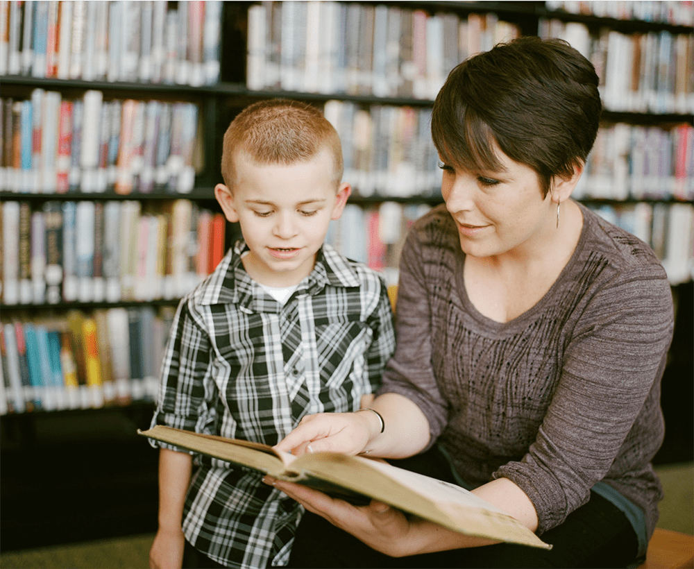 Adult and child reading together in a library.