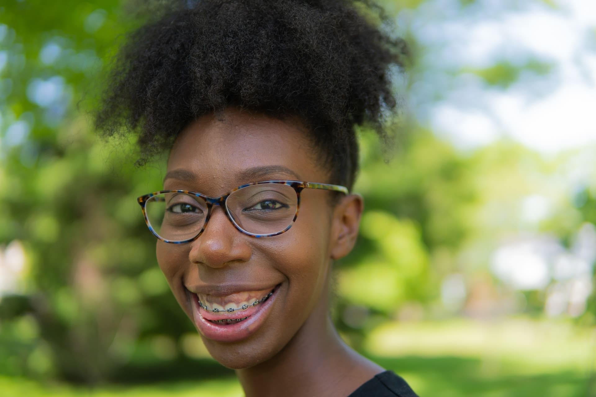 Close-up of a smiling teenager with glasses and braces, outdoors.