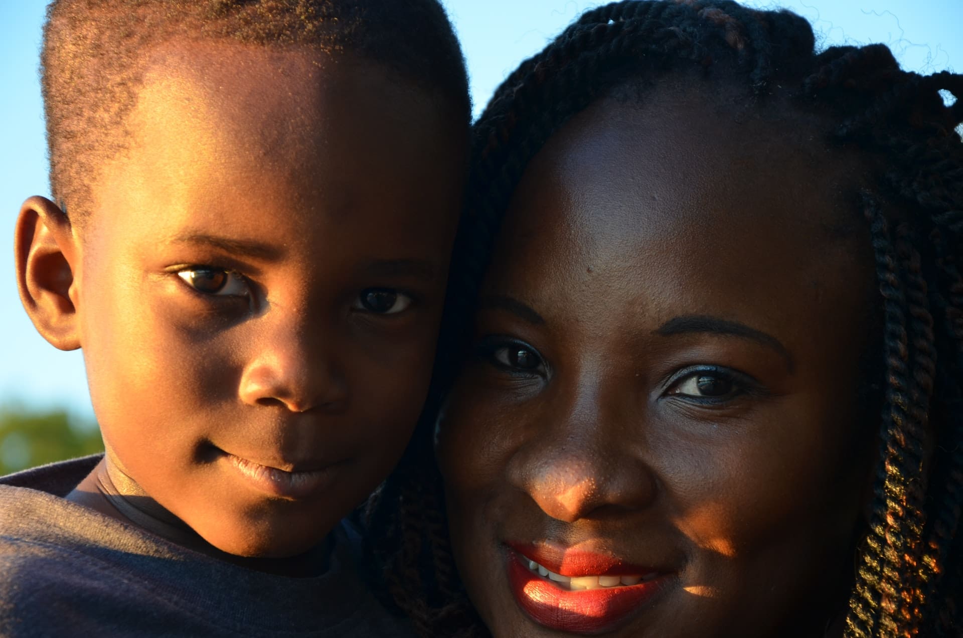 Close-up of an adult and a child, both looking at the camera, outdoors.