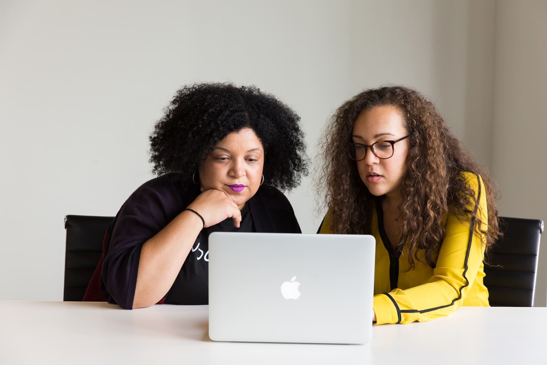 Two women looking at a laptop screen together in an office setting.