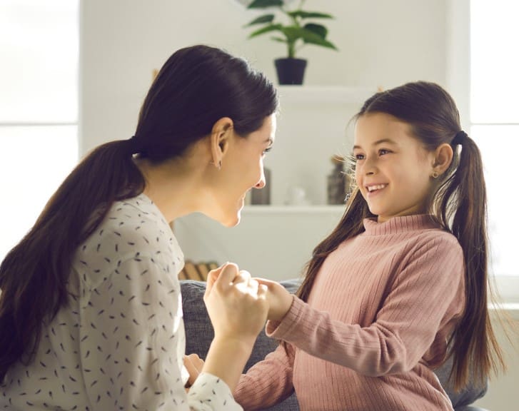 Adult and child holding hands, smiling at each other.
