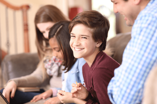 Two children and two caregivers smiling and sitting together on a couch.