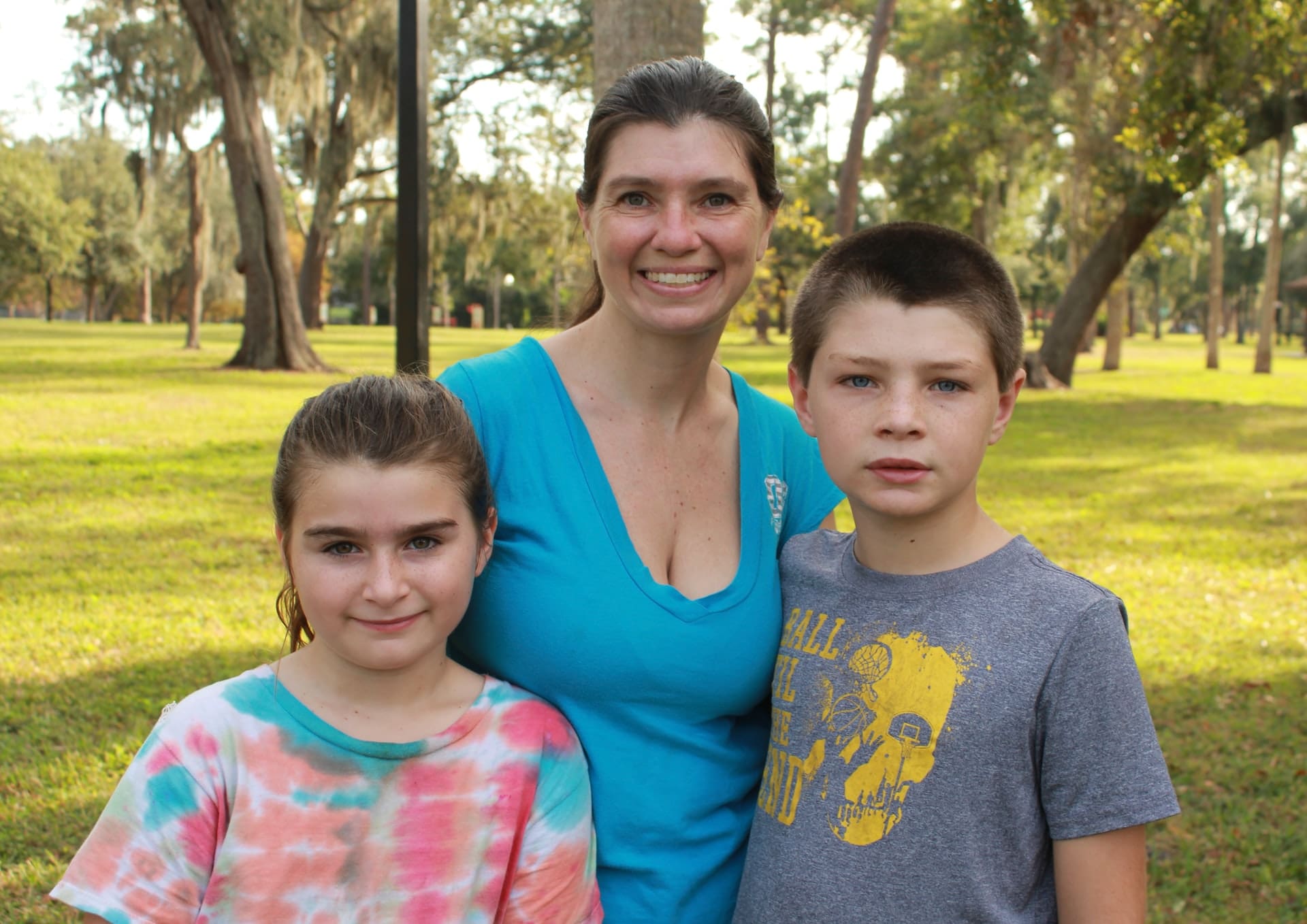 An adult with two children in a park, smiling at the camera.