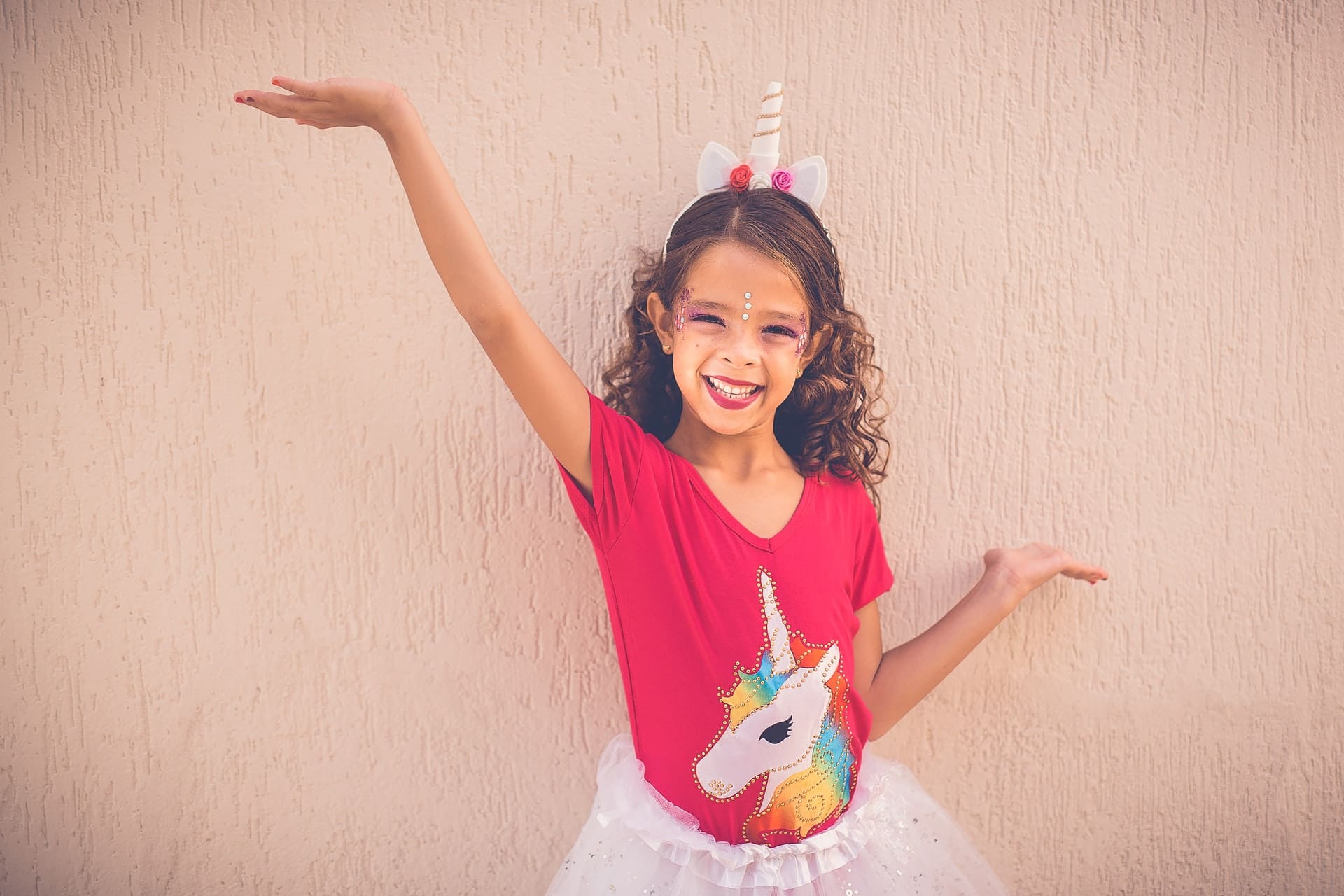 Child in a rainbow-colored unicorn shirt with face paint, smiling.