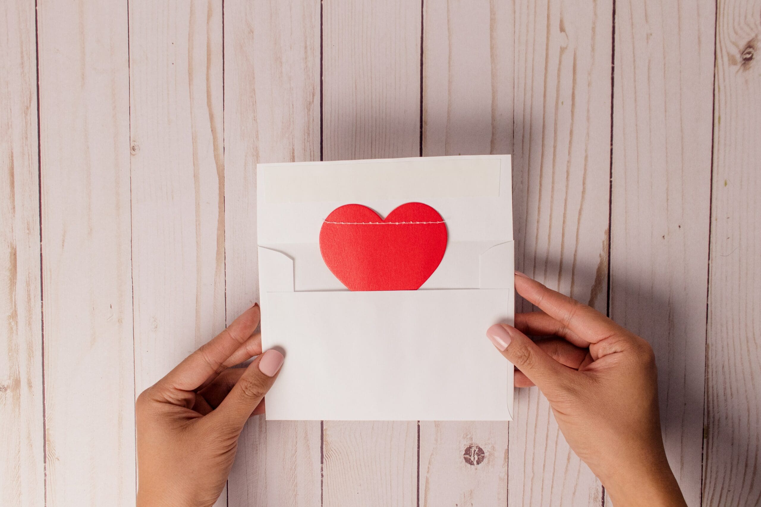Hands holding a white envelope with a red heart inside.