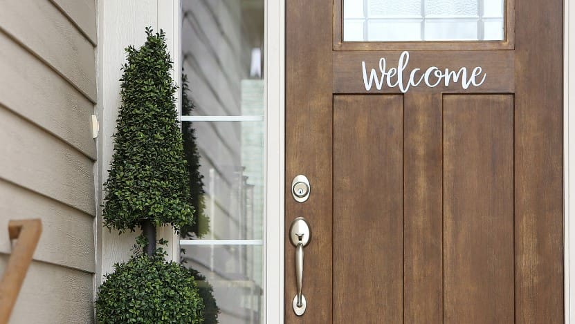 Front door with 'Welcome' sign, surrounded by greenery.