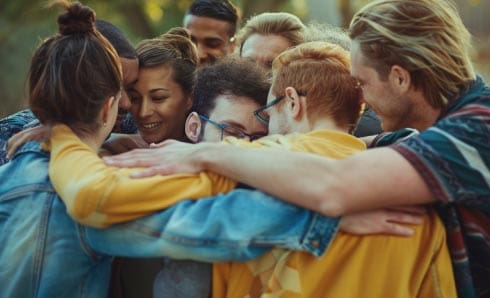 Group of diverse people embracing in a circle, smiling.