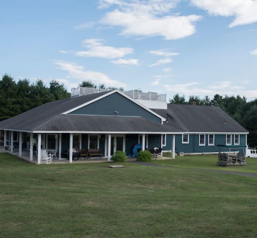 Large blue building with a porch and outdoor furniture, surrounded by grass.
