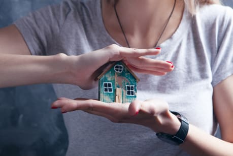 Person holding a small wooden house model in their hands