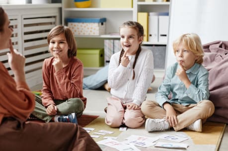 Three children sitting on the floor, listening to a teacher.