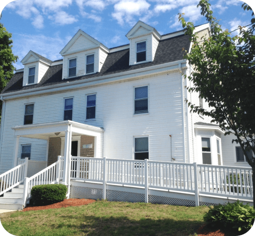 White building with a porch, stairs, and a picket fence