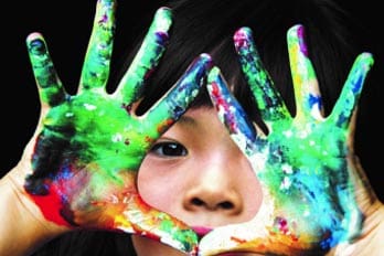 Child holding hands covered in colorful paint in front of face