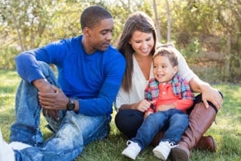 Two adults and a child sitting on grass outdoors, smiling.
