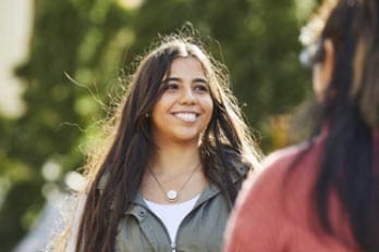 Two people talking outdoors, one smiling, the other with back turned.