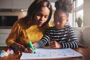 Adult and child writing on paper with markers.