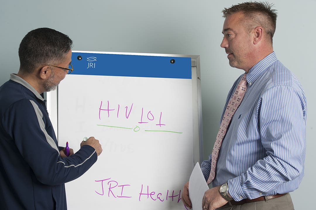 Two people in a classroom looking at a whiteboard, one writing and the other holding papers.