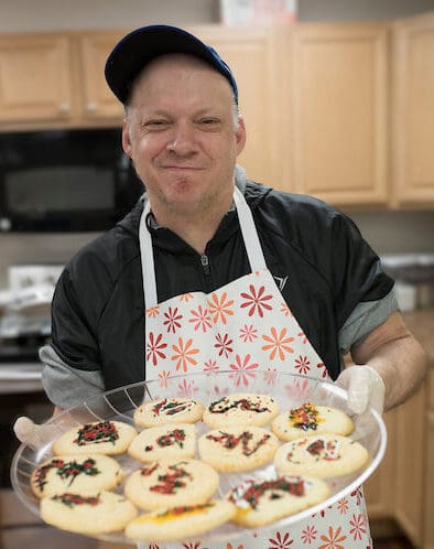 Person in apron holding tray of decorated cookies in kitchen.