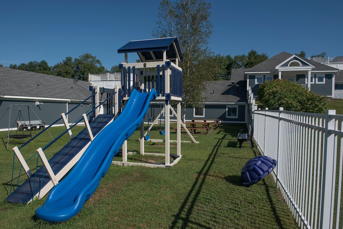 Playground with slides, swings, and a sandbox in a fenced yard