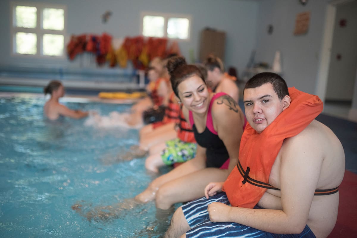People sitting on the edge of a pool, some wearing life jackets, smiling.