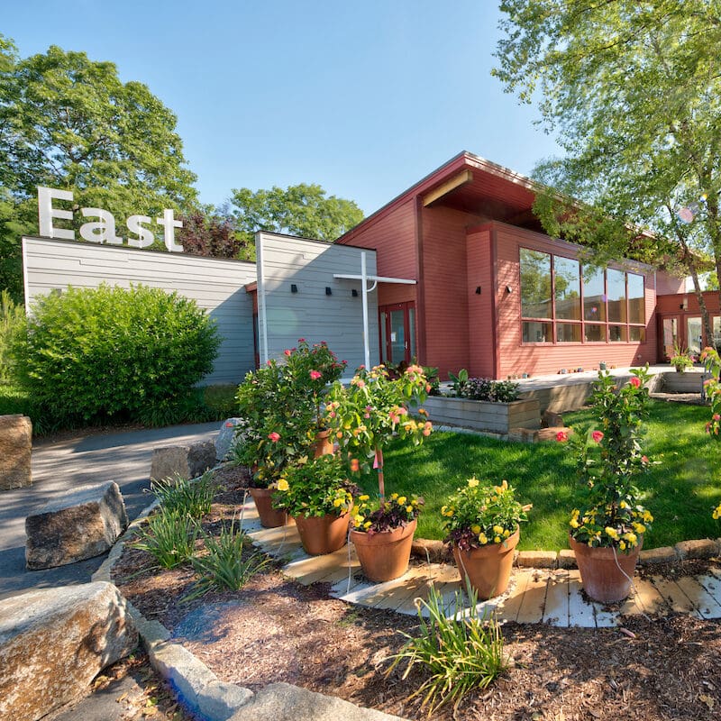 Building with large windows and a sign that says 'East' surrounded by plants.